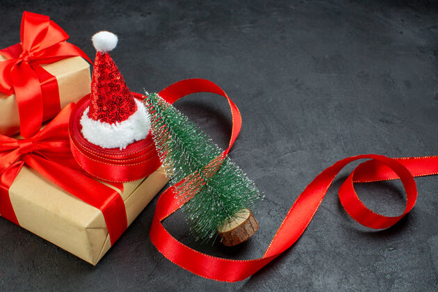 一半黑色桌子上的圣诞树上挂着红丝带和圣诞老人帽的漂亮礼物的半张照片鞋鞋帽子
