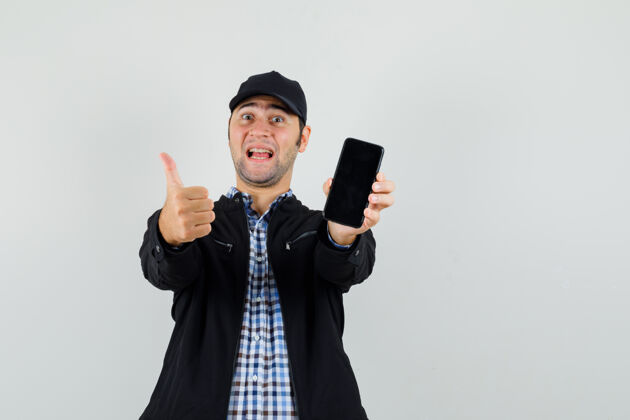 持有年轻人拿着手机 在衬衫 夹克 帽子上竖起大拇指 看上去很高兴手机成功高兴