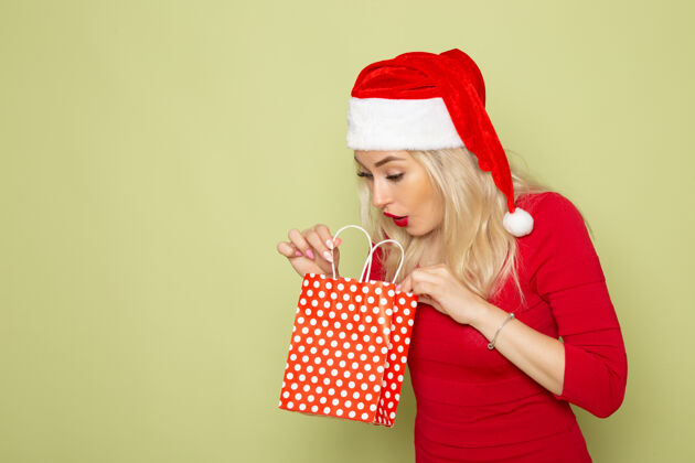 颜色正面风景美丽的女性拿着礼物在绿色的墙上小包装情感节日圣诞雪色新年小包装帽子