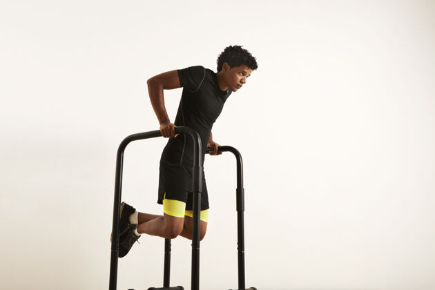 帅气一个专注的肌肉发达的非洲裔美国年轻人的肖像 穿着黑色运动服 在白色的双杠上做蘸酱Dip健康锻炼