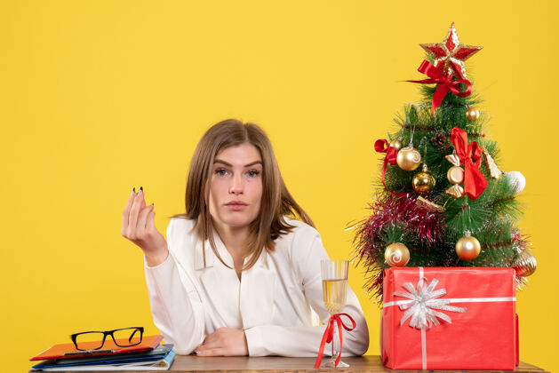 肖像正面图：女医生坐在黄色桌子上的桌子前 桌上放着圣诞树和礼品盒圣诞节漂亮微笑