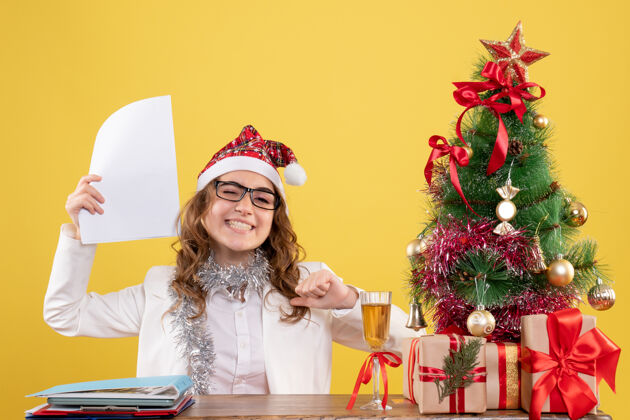 坐着前视图女医生坐在圣诞树上 拿着黄色背景上的文件鲜花庆祝礼物