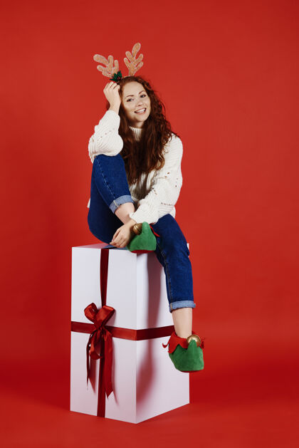 惊喜带着巨大圣诞礼物的微笑女人的画像打开购物鹿角