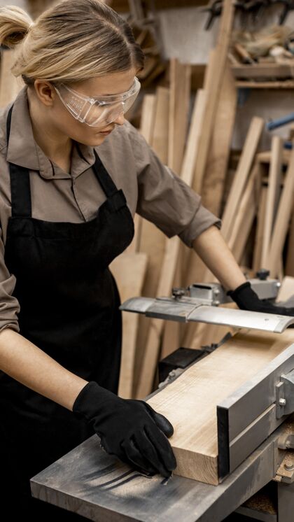 劳动带安全眼镜的女木匠锯木头技能妇女工人