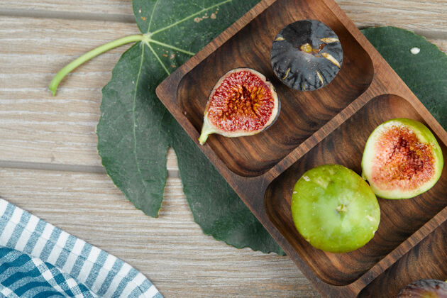 异国情调成熟的绿色和黑色无花果放在木盘上 用叶子和桌布顶木制桌布