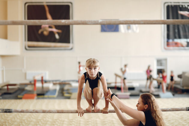 事件儿童体操平衡木女子体操运动员在体操比赛中练习单杠带着孩子的教练女人艺术赤脚