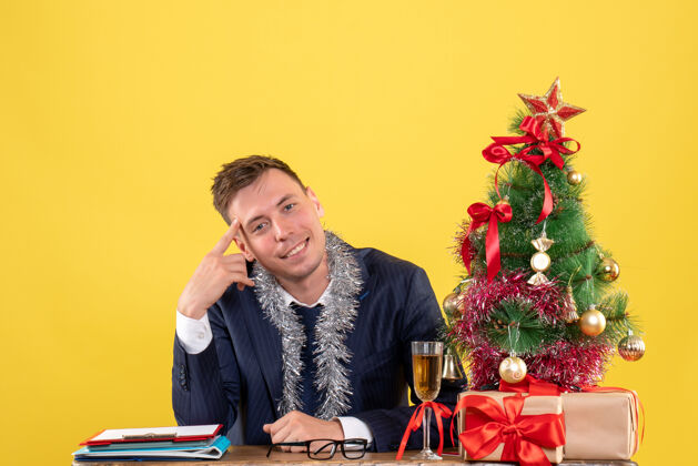男人笑容可掬的帅哥坐在圣诞树旁的桌子前 黄色的礼物礼物圣诞节帅哥