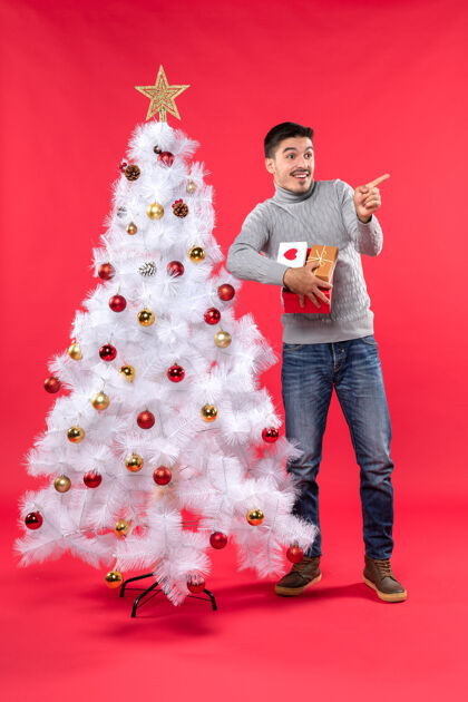 礼物站在装饰过的白色圣诞树旁 手持礼物 面带微笑的帅哥的俯视图圣诞节指着树