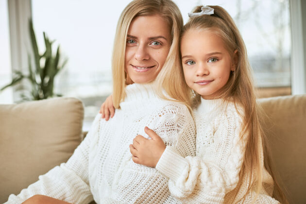 孩子室内镜头：美丽的小女孩抱着她迷人的年轻女性 双手搂在腰上 两人都穿着舒适温暖的毛衣 带着快乐的笑容 玩得开心拥抱年轻女儿