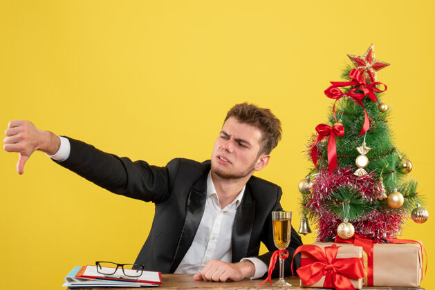圣诞节正面图坐在工作场所后面的男工人对黄色不满意男工作年