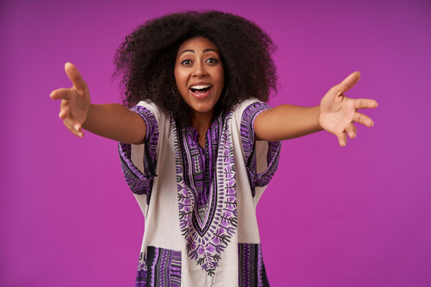 正面年轻漂亮的黑皮肤女性 随意的发型 穿着白色的图案衬衫 张开双臂在紫色的衣服上摆姿势 准备拥抱快乐紫色非洲