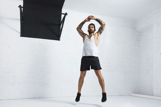 胸部纹身和肌肉运动员做跳跃杰克隔离在白色砖墙旁边的黑色拉杆区域健美操活跃