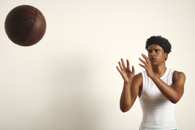 投掷强壮严肃的黑人运动员 穿着一件纯白色无袖衫的非洲裔 在白色衣服上扔一个深棕色的老式篮球冠军运动员球