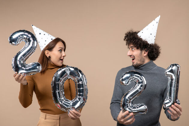 肖像快乐的年轻夫妇戴新年帽为摄像女孩摆姿势男人圣诞节情侣