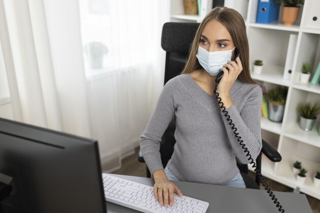 医疗面罩怀孕的女商人在办公桌边打电话 戴着医用口罩女性母亲医疗