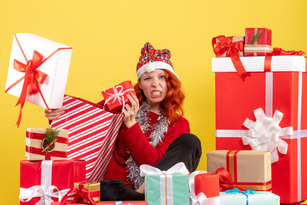 礼物坐在黄色墙上的圣诞礼物周围的年轻女子的正视图盒子购物礼物