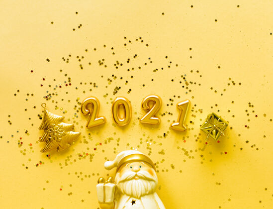 五彩纸屑玩具圣诞老人与一个金色的礼品盒和铭文2021年的黄色背景假日概念 顶视图 复制空间2021年扁平年份