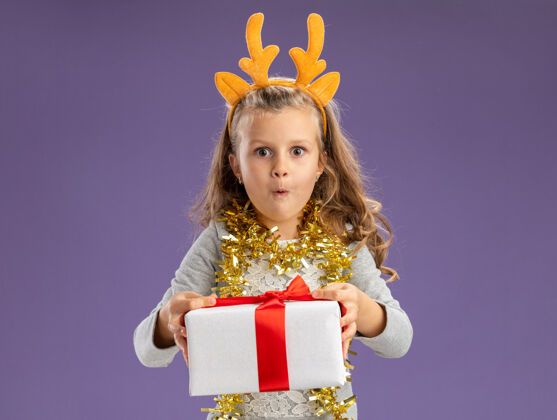 箍兴奋的小女孩戴着圣诞发箍 脖子上戴着花环 手里拿着礼品盒 孤零零地站在蓝色的墙上穿脖子小