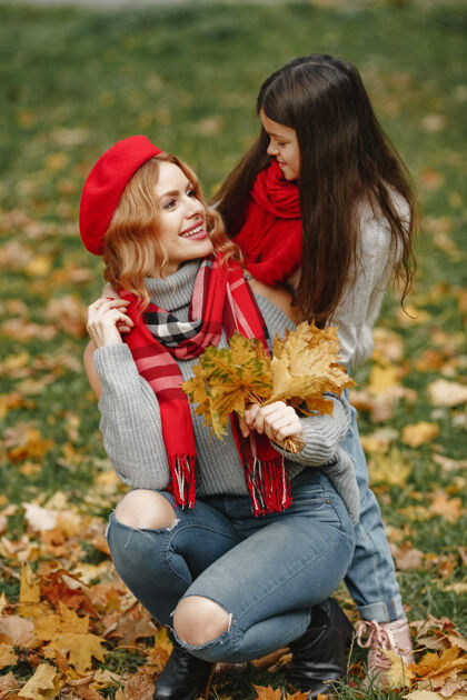 户外时髦的母亲带着女儿黄色的秋天戴着红领巾的女人女孩秋天围巾