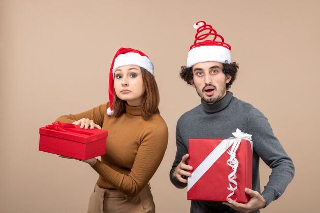 帽子新年气氛和派对概念的俯瞰图-戴着圣诞老人帽子拿着礼物的迷茫可爱的情侣心情礼物上衣