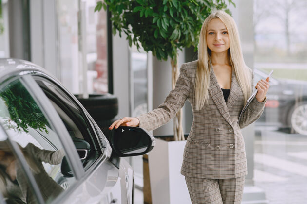 经销商汽车沙龙里的女士买车的女士穿着棕色西装的优雅女士展示女人微笑