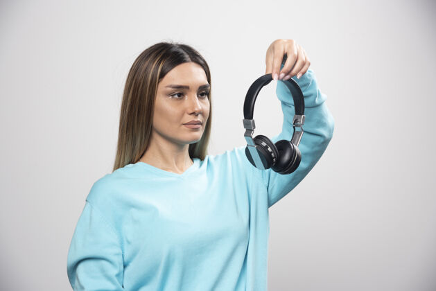 员工穿着蓝色运动衫的金发女孩拿着耳机 准备戴上耳机听音乐聪明积极表演