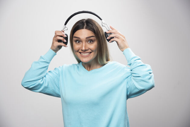 积极穿着蓝色运动衫的金发女孩拿着耳机 准备戴上耳机听音乐年轻人音乐家休闲