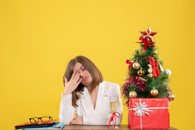 人正面图：女医生坐在黄色桌子上的桌子前 桌上放着圣诞树和礼品盒情感肖像快乐