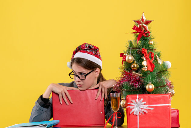 鸡尾酒前视图体贴的女孩戴着圣诞帽坐在桌旁圣诞树和礼物鸡尾酒体贴的女孩服装女孩