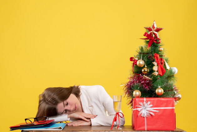 健康正面图：女医生坐在桌子前 睡在黄色背景上 还有圣诞树和礼品盒桌子医生圣诞节