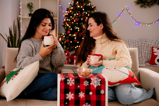 圣诞节微笑着的年轻女孩抱着杯子看着坐在扶手椅上的杯子 在家里享受圣诞节时光快乐时间家