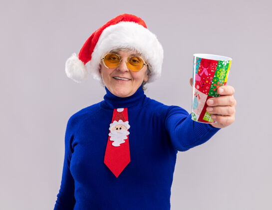 太阳戴着太阳眼镜 戴着圣诞帽 打着圣诞领带 手里拿着纸杯 面带微笑的老妇人圣诞快乐女人新年