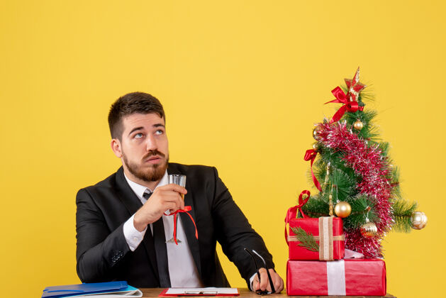 树正面图：一位男性工人在他的桌子后面 黄色的圣诞树上放着礼物和圣诞树男西装男工人