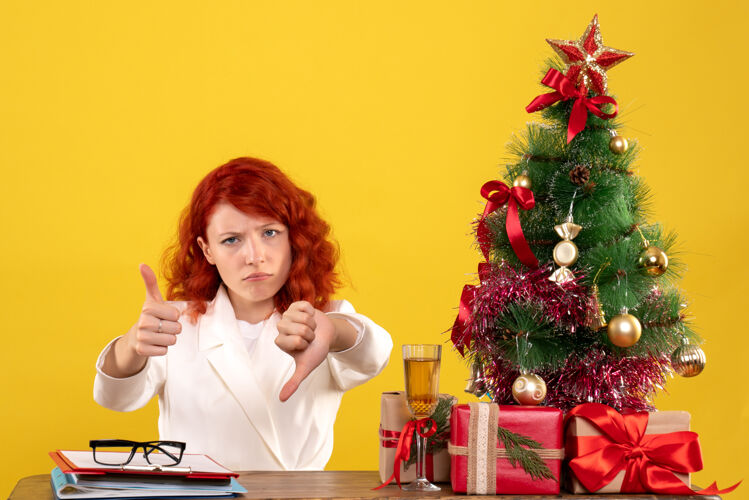 礼物女工人坐在桌子后面 手里拿着圣诞礼物和黄色的圣诞树办公室桌子安排