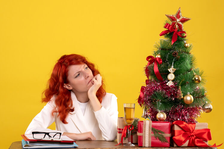 女工人女工人坐在桌子后面 手里拿着圣诞礼物和黄色的圣诞树圣诞节办公室黄色