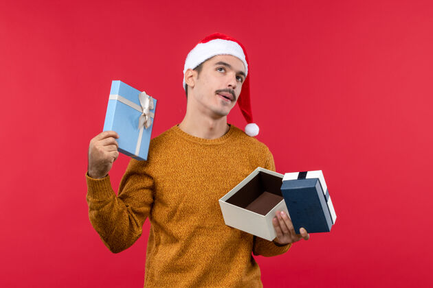 圣诞节红墙上拿着礼品盒的年轻人的正视图微笑礼物人