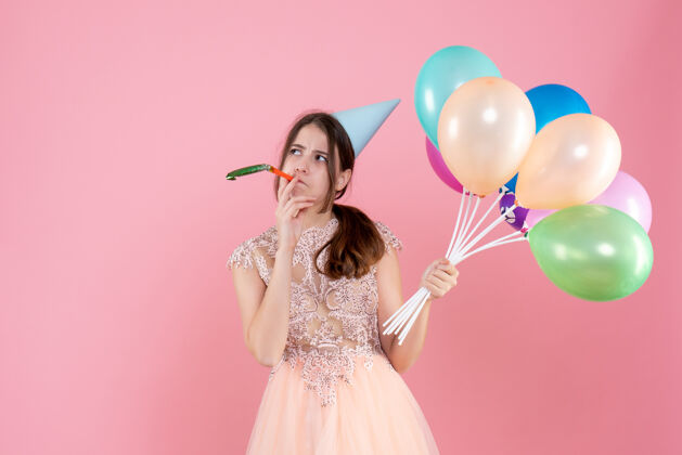 聚会脾气暴躁的派对女孩 戴着派对帽 手里拿着气球 在粉色上用隔音器生日粉红色乐趣