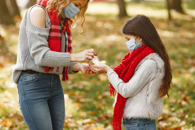大流行秋天公园里的一家人冠状病毒主题母亲带女儿人们用杀菌剂贝雷帽孩子面具