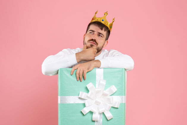 男性礼物盒内年轻人的正面图 头戴皇冠 在粉红色的墙上思考聚会皇冠游戏