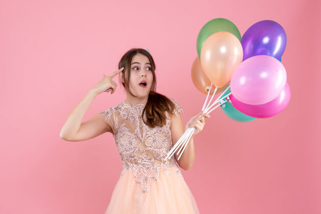 时尚看着戴着派对帽的派对女孩拿着粉色的气球气球观察举行