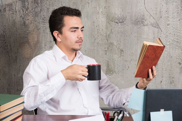 商人年轻的商人在书桌上看书喝茶阅读杯子人