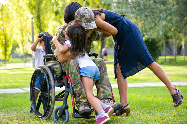 军队孩子们和他们的妈妈拥抱着公园里的残疾退役军人父亲退伍军人还是回家的概念父母椅子返回