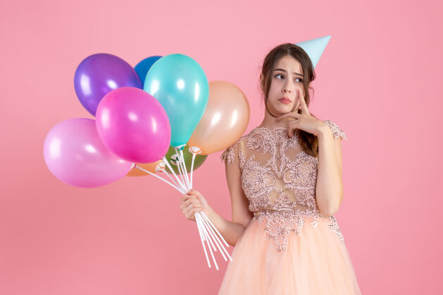 派对戴着派对帽的悲伤女孩拿着气球把手指放在粉色的脸颊上气球公主贵族