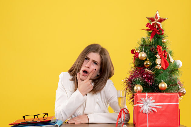 医院正面图：女医生坐在黄色背景的桌子前 放着圣诞树和礼品盒女性健康圣诞节