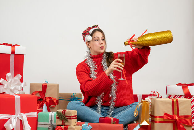 成人戴着圣诞帽的年轻女孩正在倒香槟 围坐在白色的礼物旁边圣诞节年轻女孩圣诞老人