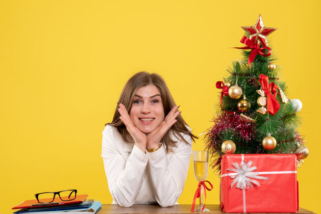 成人正面图：女医生坐在黄色背景的桌子前 放着圣诞树和礼品盒人医院圣诞节
