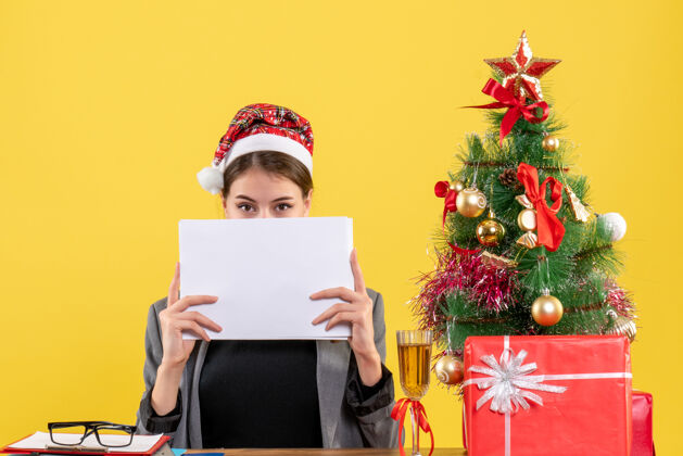 树正面图：戴圣诞帽的年轻女孩坐在桌旁 脸上贴着圣诞树和鸡尾酒礼物桌子礼物鸡尾酒
