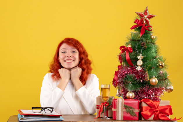 人正面图：女医生坐在桌子后面 黄色背景上带着微笑的圣诞礼物快乐人桌子
