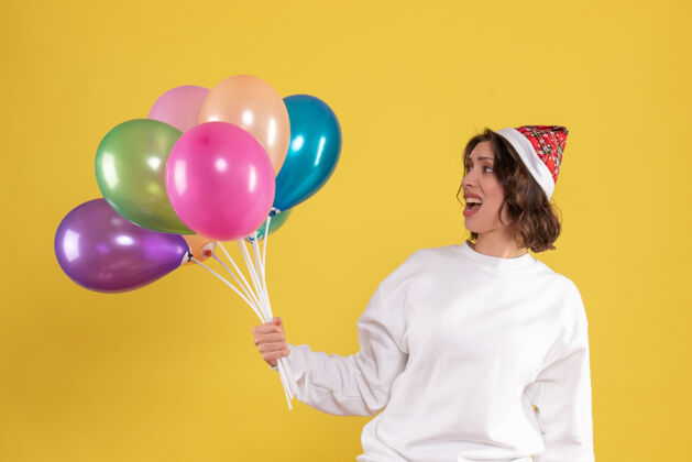 气球黄色墙壁上手持彩色气球的年轻女子的正视图节日生日庆祝