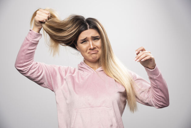女性穿着粉色运动衫的金发女士对自己的干枯头发或发色感到不满意人年轻人护发用品